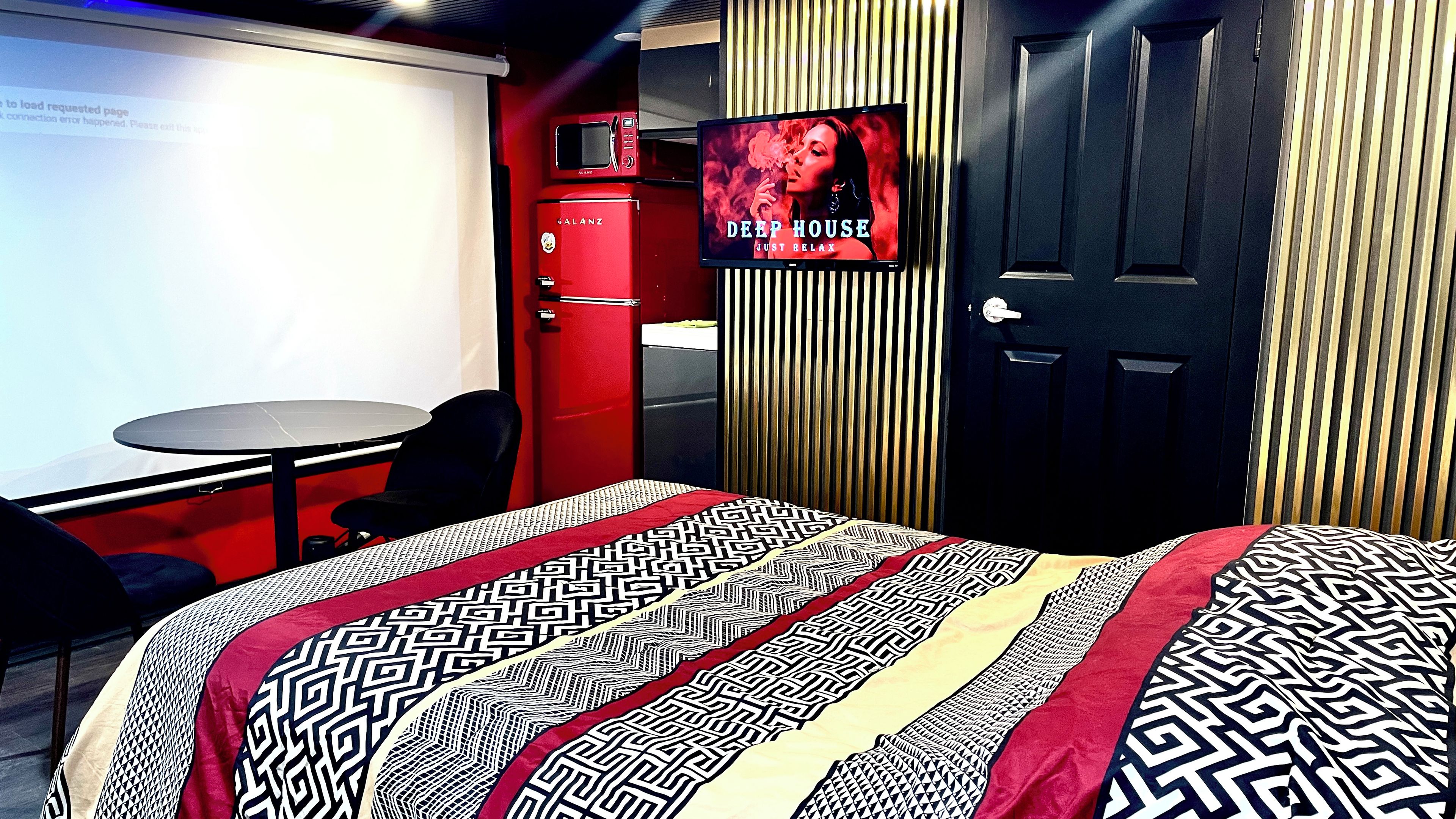 A hotel room with a bed, a desk, a chair, a TV, and a door.