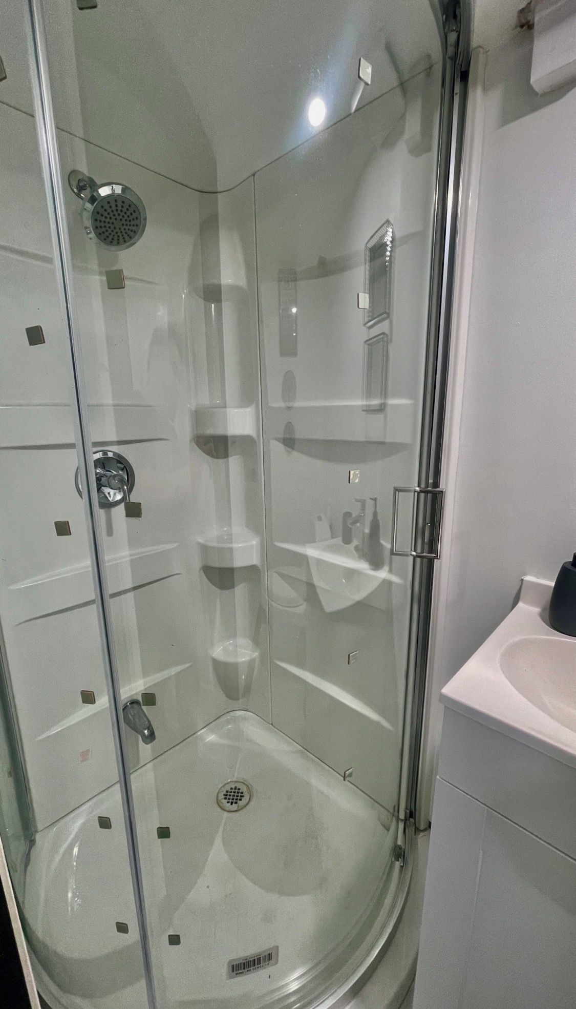 Eine begehbare Dusche mit Glaswänden, einer Handbrause, einer Glastür und einem weißen Waschbecken inklusive Spiegel.