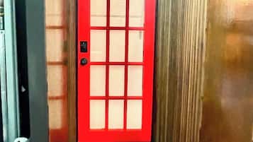 A red door with a grid pattern, a small step leading up to it, and a wall with vertical lines.