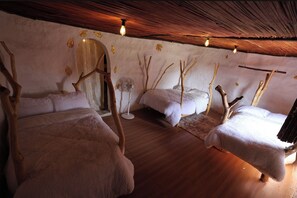 Quarto com três camas, um ventilador e teto rústico.