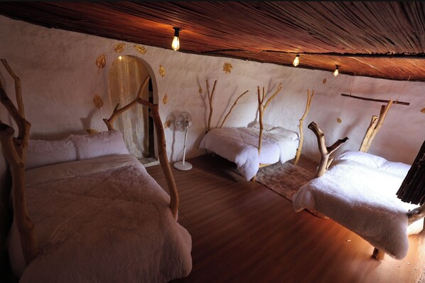 A room with three beds, a fan, and a rustic ceiling.