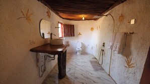 A bathroom with a marble floor, a sink with a mirror, a toilet, and a shower area. - Maasai Heritage Museum (Kajiado County)