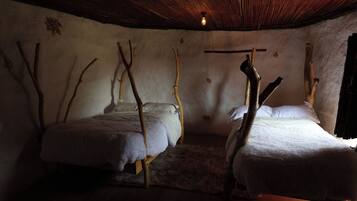 A room with two beds, each supported by wooden branches, and a rustic ceiling.