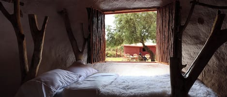 A rustic room with a bed, a window with curtains, and a view of the outside.
