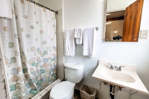 Un baño con inodoro, lavabo, espejo y cortina de ducha con diseño de conchas marinas.