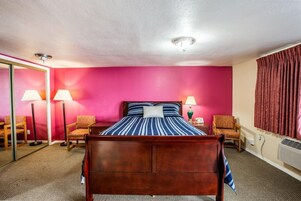 Una habitación de hotel con una cama de madera, dos sillas, un espejo y una pared roja.