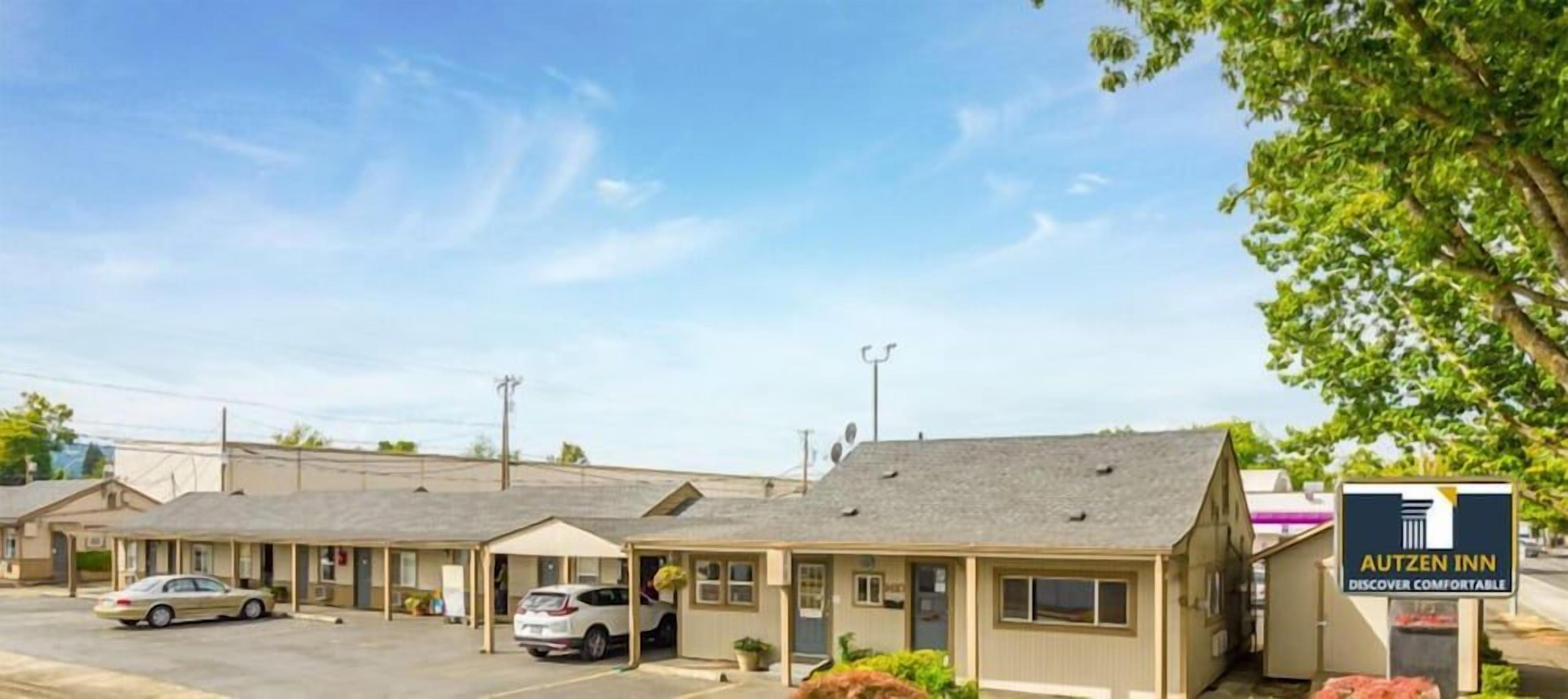 Um motel com construção térrea, estacionamento e placa indicando o nome 'AUTZEN INN'.