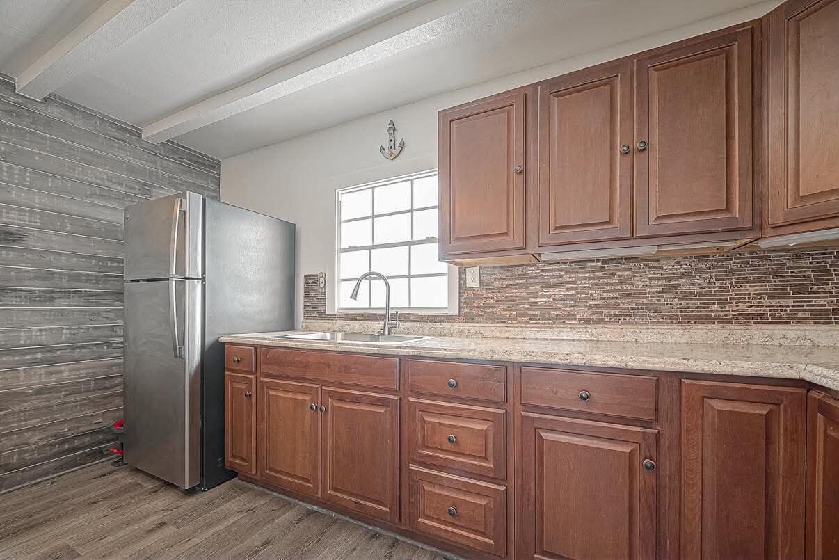A kitchen with wooden cabinets, a stainless steel refrigerator, and a window with a view.