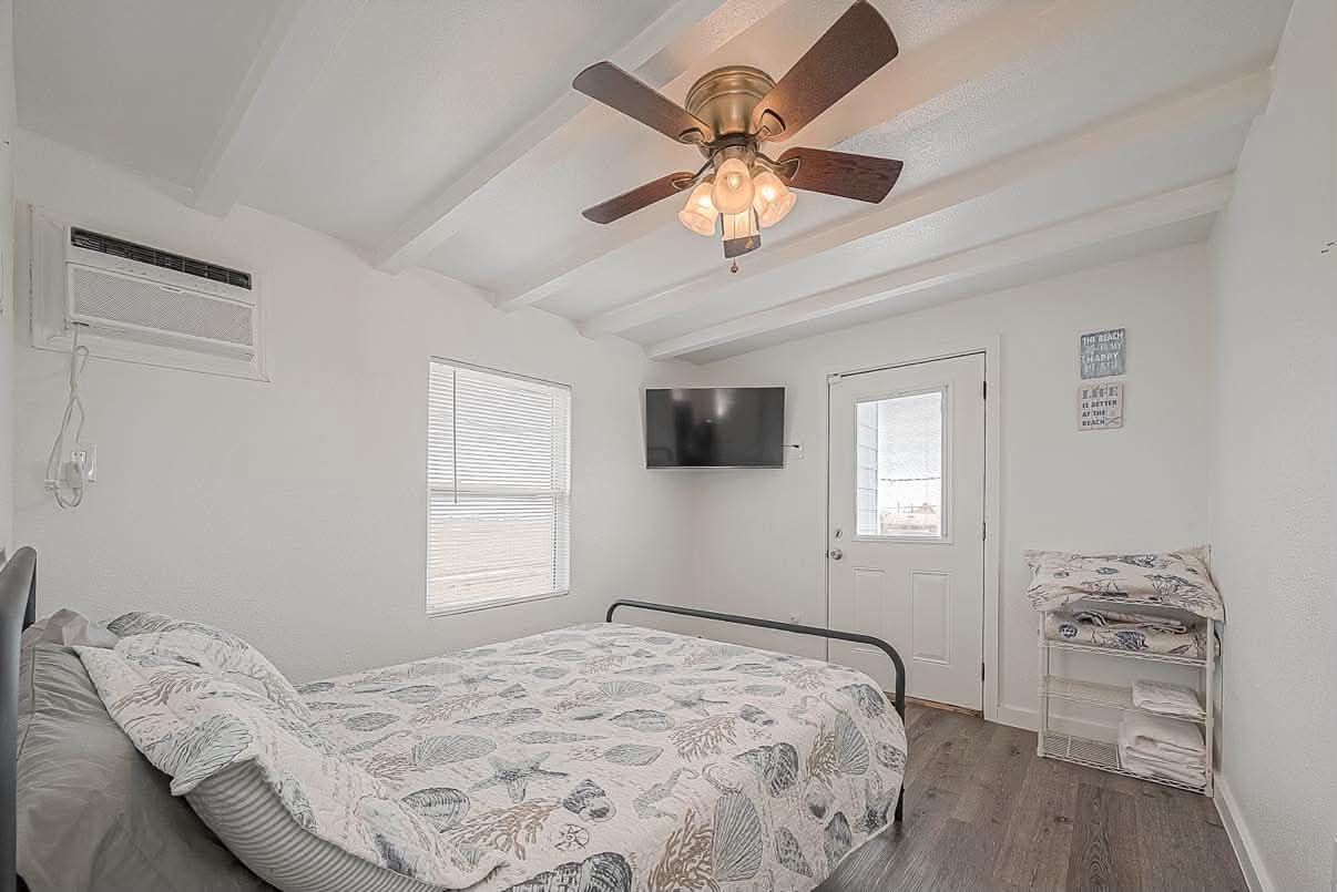 A bedroom with a bed, a ceiling fan, a TV, and a window.