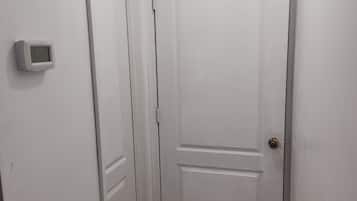 A white door with a digital thermostat and a vent on the wall.