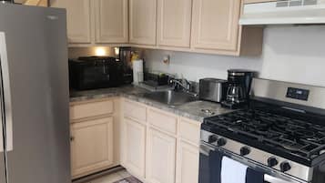 A kitchen with light-colored cabinets, a stainless steel refrigerator, a microwave, a stove, and a coffee maker.