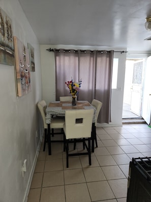 Ein Essbereich mit Tisch für vier Personen, einem Blumenstrauß und Blick durch ein mit Vorhängen drapiertes Fenster.