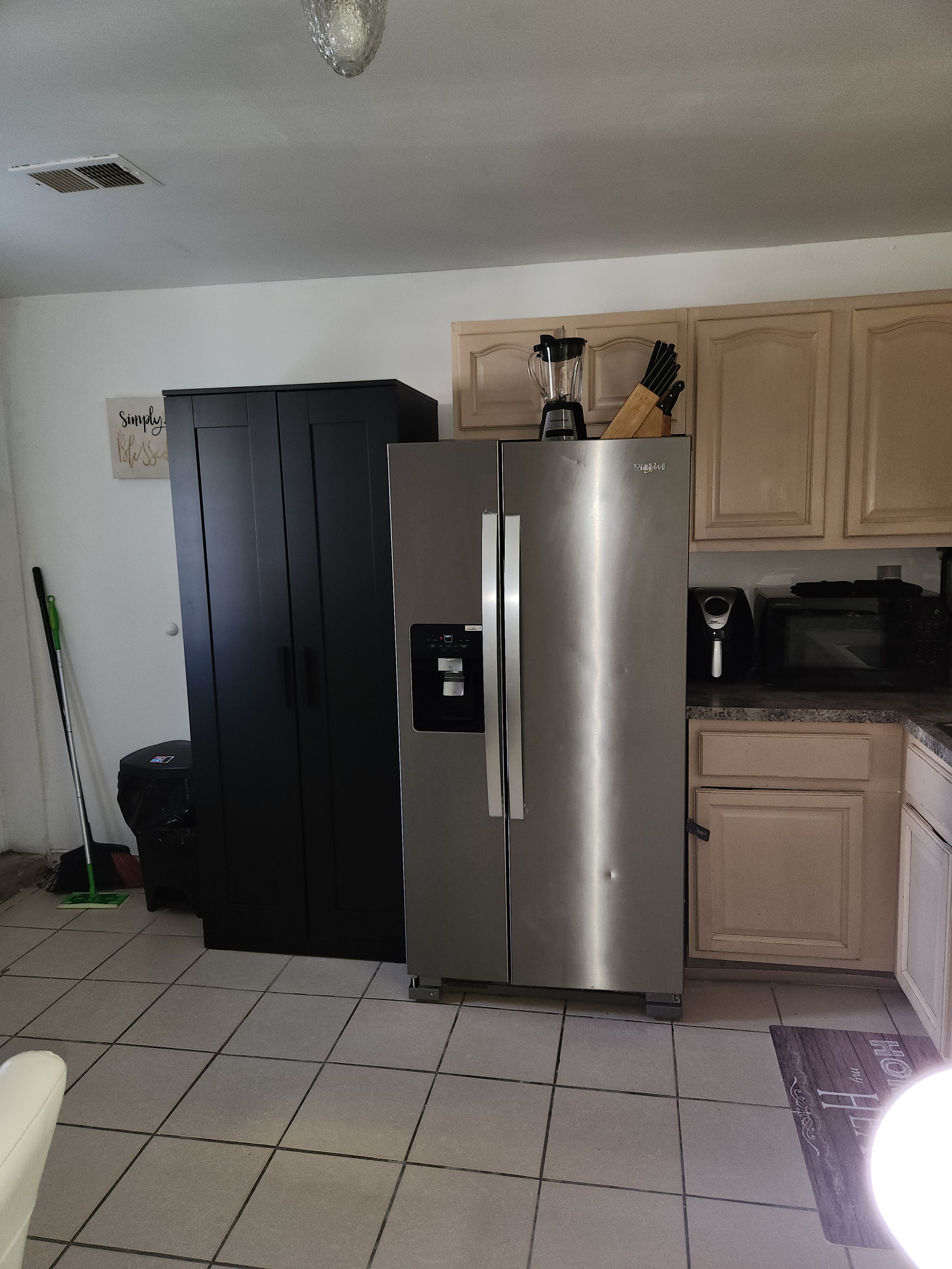 A kitchen with a stainless steel refrigerator, a black cabinet, and a wooden countertop.