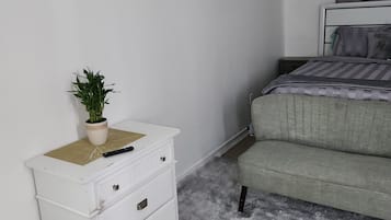 A bedroom with a bed, a white dresser with drawers, a fluffy rug, and a potted plant.