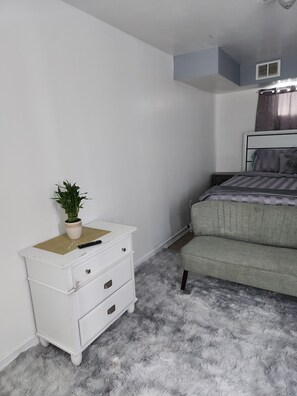 A bedroom with a bed, a white dresser with drawers, a fluffy rug, and a potted plant. - A Home Away from Home. (Staten Island)
