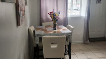 A dining area with a table set for two, a vase of flowers, and a window with curtains.