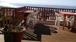 Eine Holzterrasse mit Sitzgelegenheiten im Freien, mit Blick auf die Küste.
