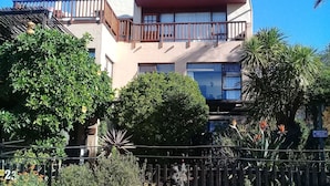 Ein zweistöckiges Gebäude mit Balkon, umgeben von Grünflächen und einem Zaun.