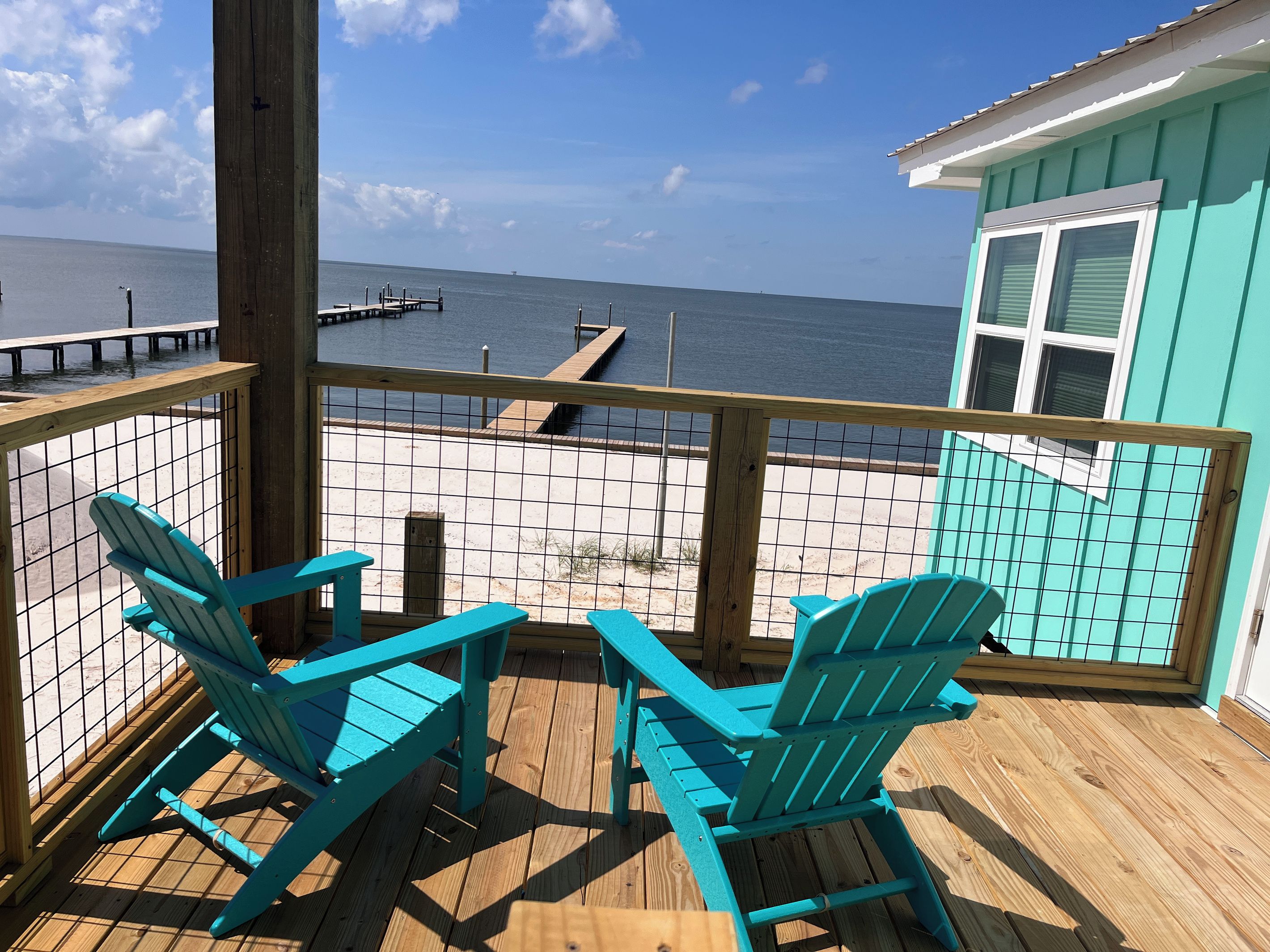 Une terrasse en bois avec deux chaises, une vue sur la mer et une jetée en arrière-plan.