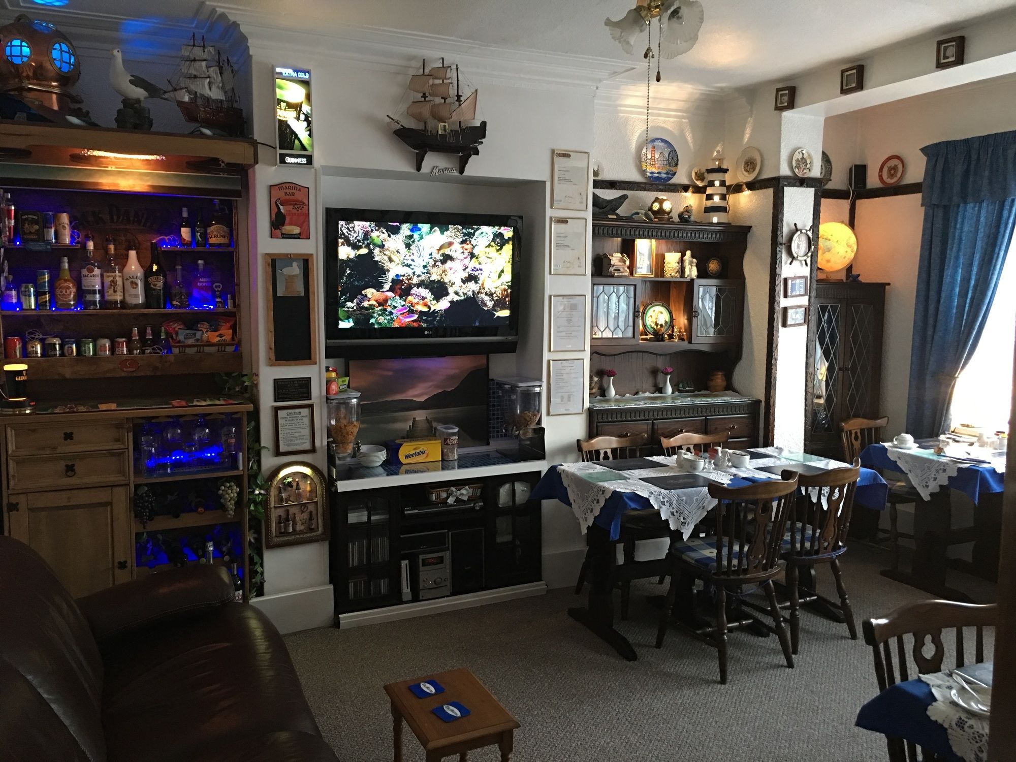 A bar area with shelves of liquor bottles, a television mounted above a bar counter, and a dining area with a table set for two.