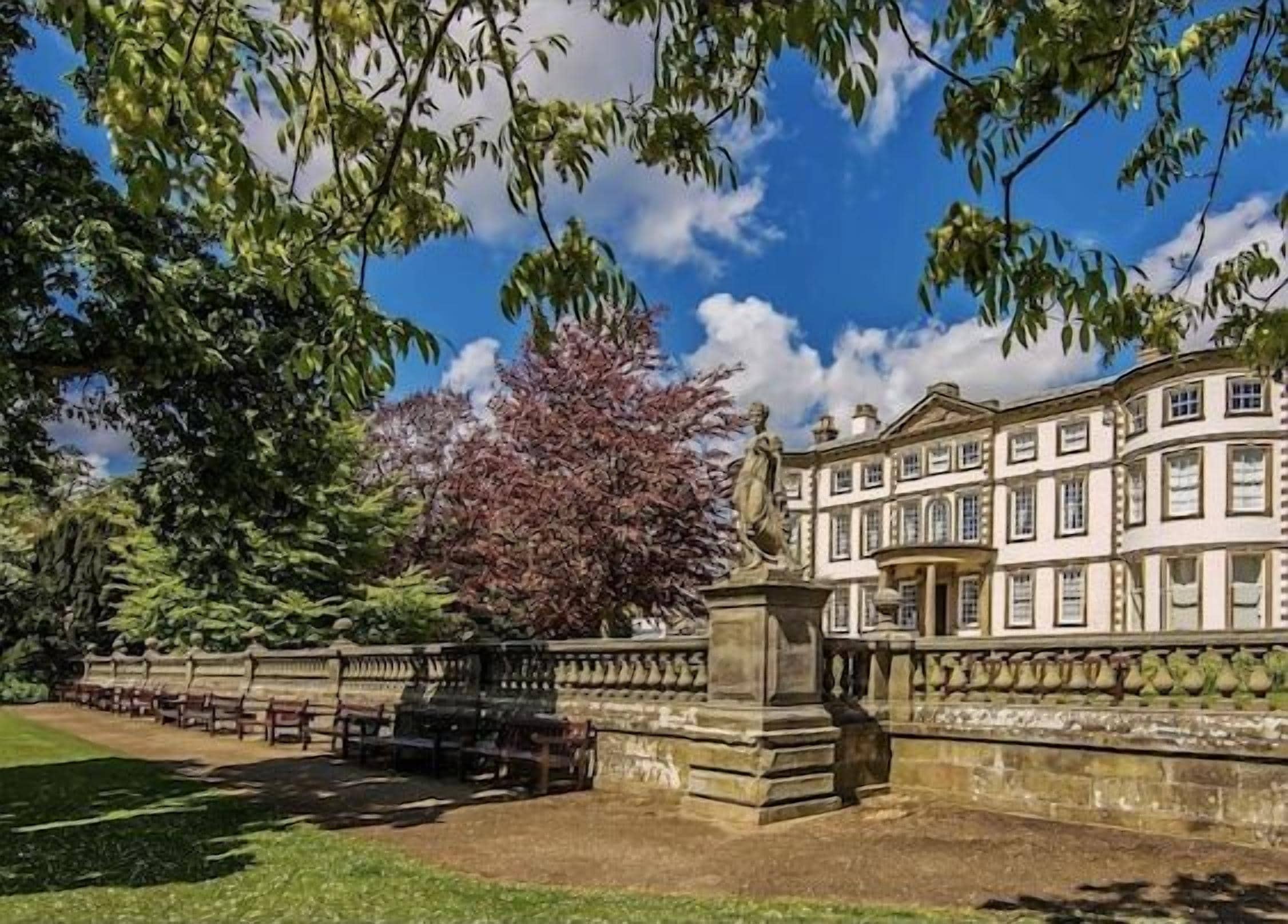 A classical building with a symmetrical facade, a central statue, and a well-maintained lawn.