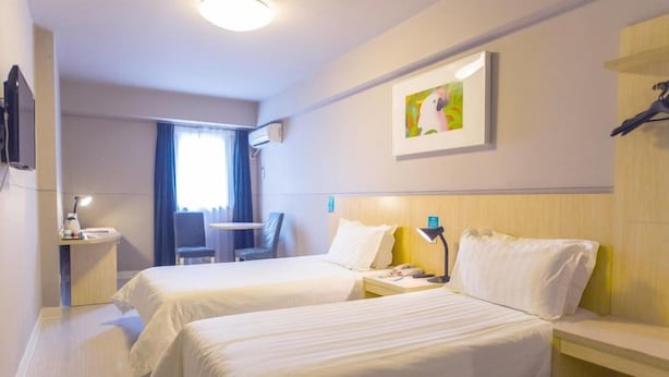 Habitación de hotel con dos camas, un escritorio con silla, un televisor y un cuadro en la pared.