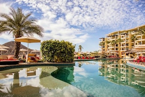 Ein Poolbereich eines Resorts mit klarem Pool, Liegestühlen, Sonnenschirmen und einem Gebäude mit Balkonen.