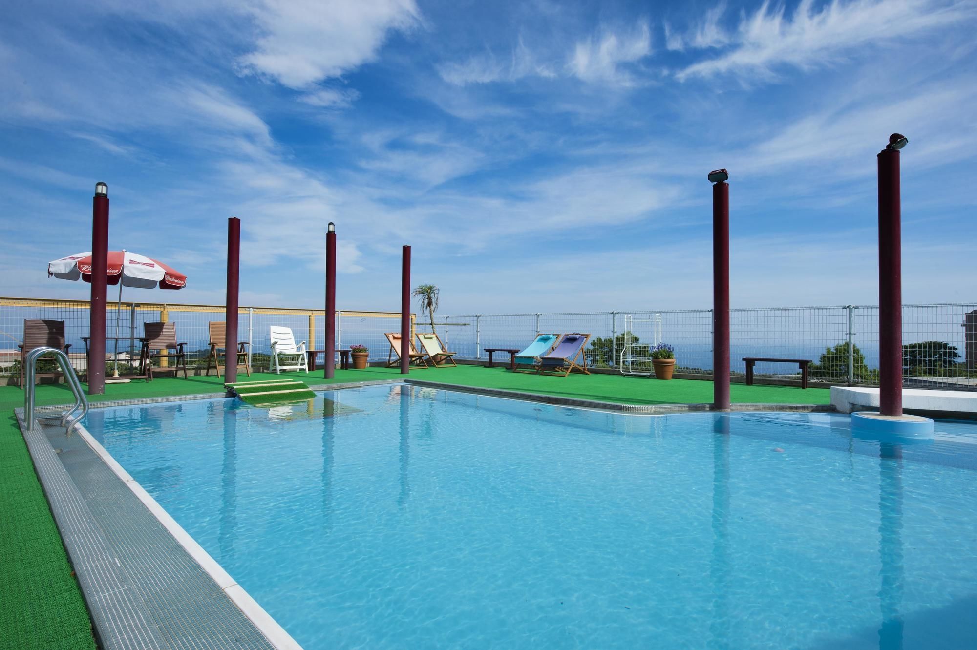 Ein Swimmingpool mit blauem Himmel, Liegestühlen und Blick auf das Meer.