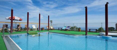 Ein Swimmingpool mit blauem Himmel, Liegestühlen und Blick auf das Meer.