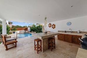 A spacious outdoor kitchen area with a pool, wooden furniture, and a view of a residential area. - Hibisca Signature Residence with 3 Bedrooms - 2 Baths + Pool (Grote Berg)