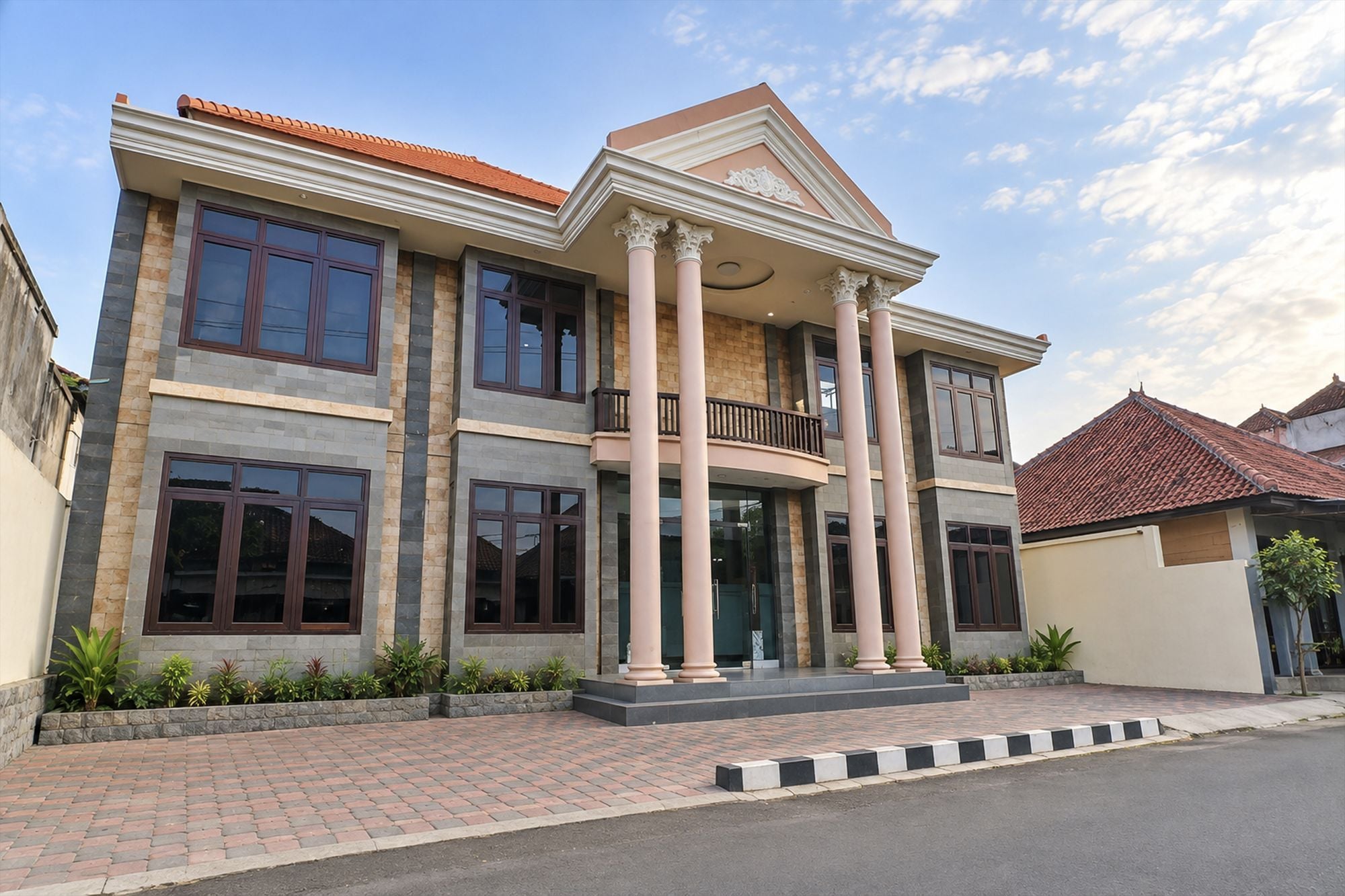 A multi-story building with a balcony, large windows, and a paved entrance area.