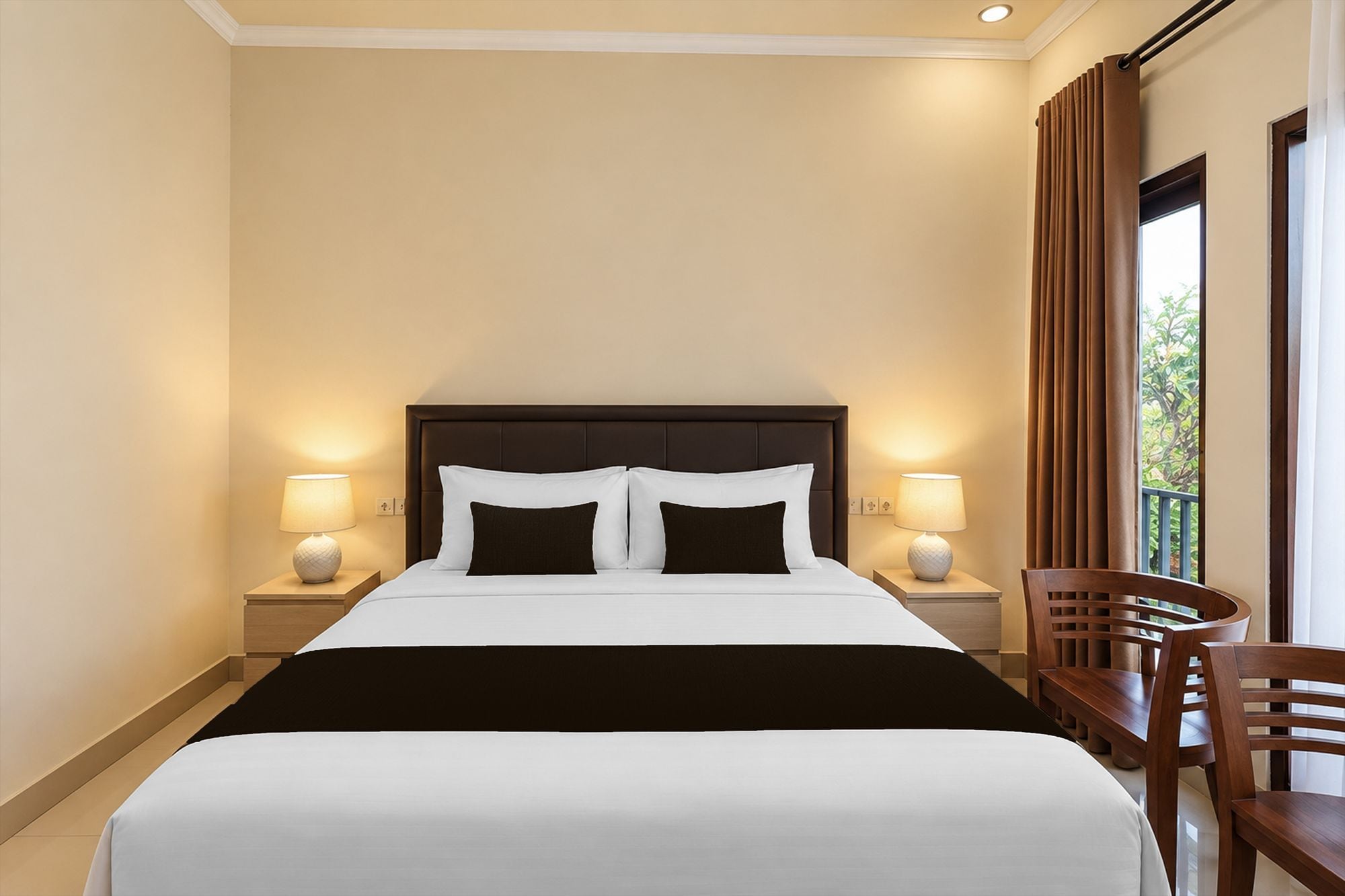 A hotel room with a large bed, two bedside lamps, a wooden chair, and a view of greenery through the window.