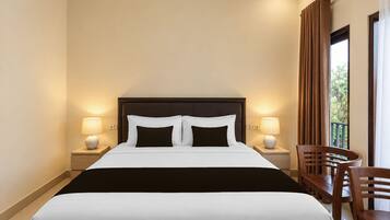 A hotel room with a large bed, two bedside lamps, a wooden chair, and a view of greenery through the window.