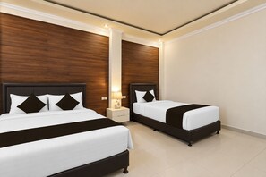 A hotel room with two beds, wooden paneling on the walls, a nightstand with a lamp, and a tiled floor.