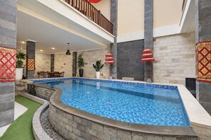 An indoor swimming pool with a tiled floor, surrounded by stone walls and a balcony with a railing.