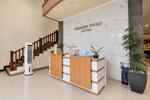 Un mostrador de recepción de hotel con una pared de mármol, una escalera de madera y una barra de recepción.
