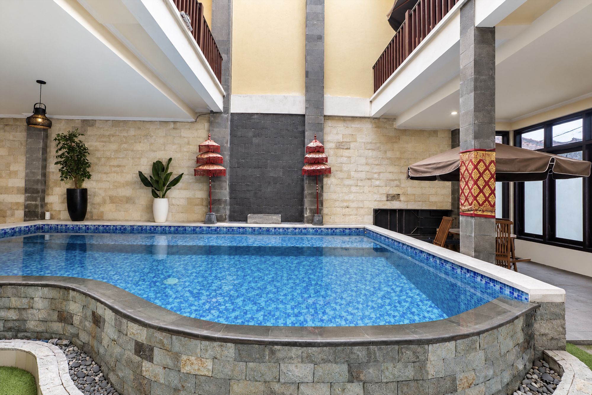 Una piscina interior con borde de azulejos, rodeada de muros de piedra, y una chimenea de piedra.