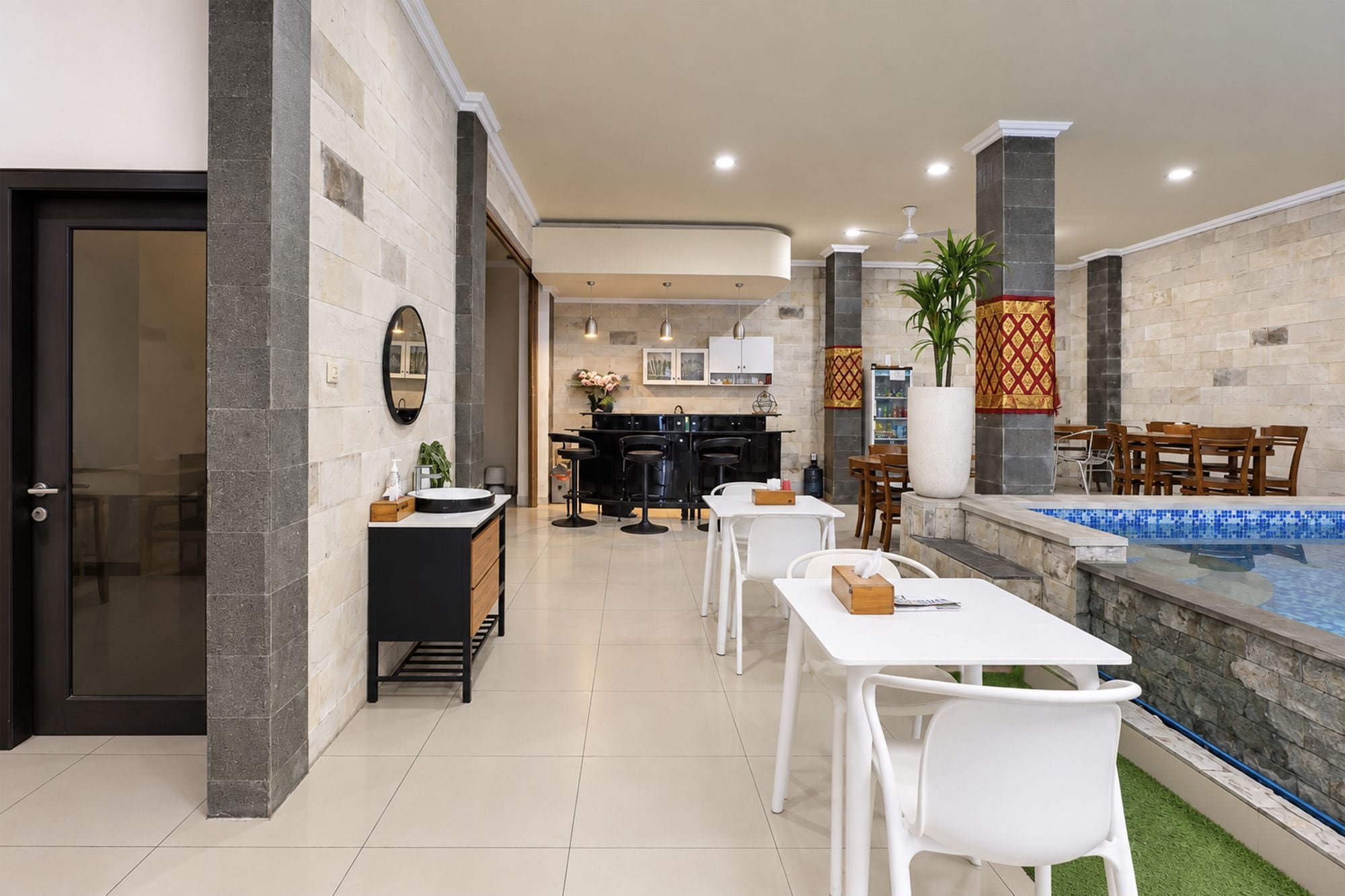 A modern kitchen with a central island, a dining area with white chairs, and a poolside seating area with a view of the pool.