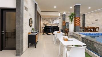 A modern kitchen with a central island, a dining area with white chairs, and a poolside seating area with a view of the pool.