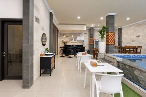 Une cuisine moderne avec un îlot central, un coin repas avec des chaises blanches et un espace détente au bord de la piscine, offrant une vue sur celle-ci.