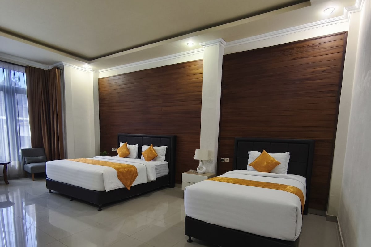 Habitación de hotel con dos camas, una mesita de noche, una lámpara y vistas al exterior.