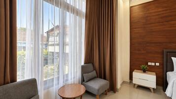 A hotel room with a bed, a small table, a chair, a nightstand, and a view of the outside.