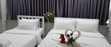 Une chambre d’hôtel avec deux lits, une grande fenêtre avec des rideaux, un vase rempli de fleurs et un ours en peluche sur l’un des lits.