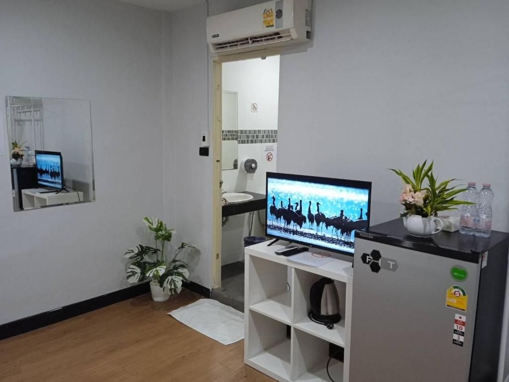 Habitación de hotel con televisor sobre un mueble, refrigerador, lavamanos y espejo.