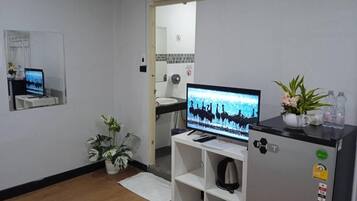 Habitación de hotel con televisor sobre un mueble, refrigerador, lavamanos y espejo.