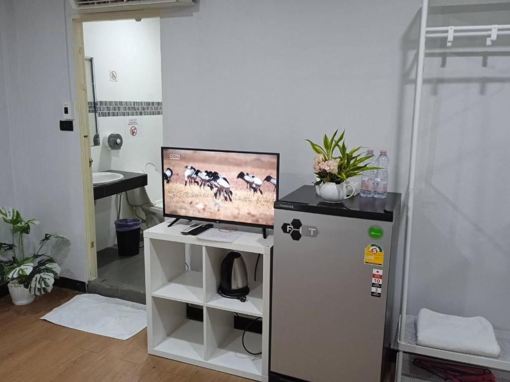 Habitación compacta con televisión, refrigerador, lavamanos y un pequeño estante.