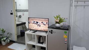 Habitación compacta con televisión, refrigerador, lavamanos y un pequeño estante.