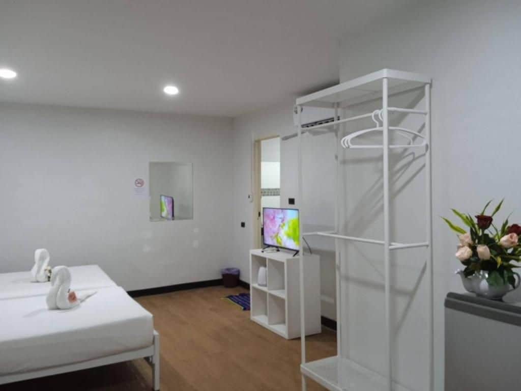 A room with a bed, a TV, a white wardrobe, and a small shelf with a flower vase.