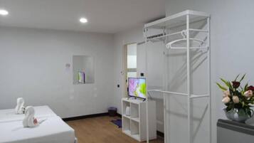 A room with a bed, a TV, a white wardrobe, and a small shelf with a flower vase.