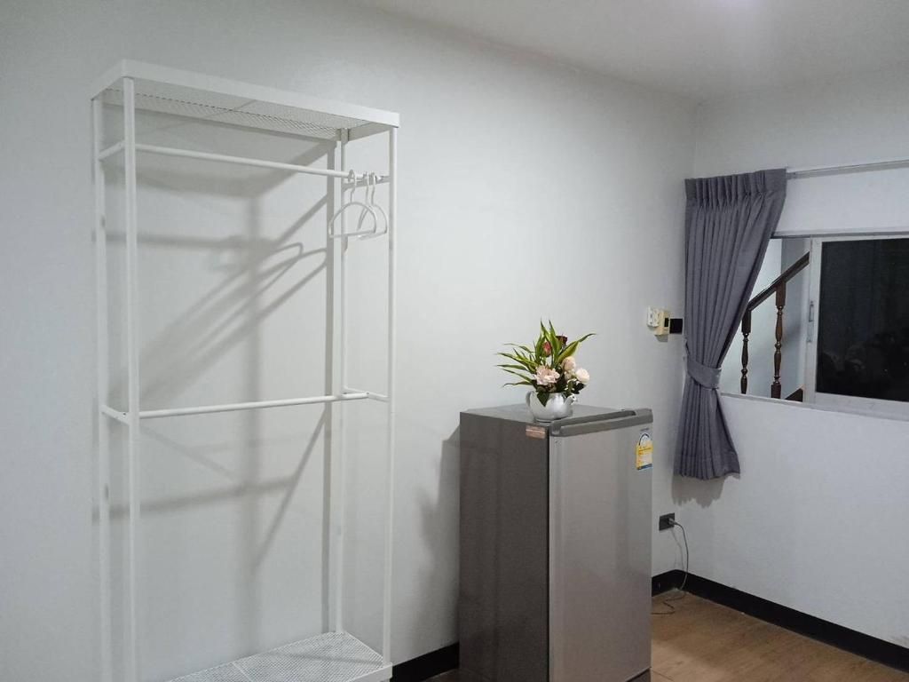 Una habitación con un armario metálico blanco, un refrigerador gris y una ventana con cortina.